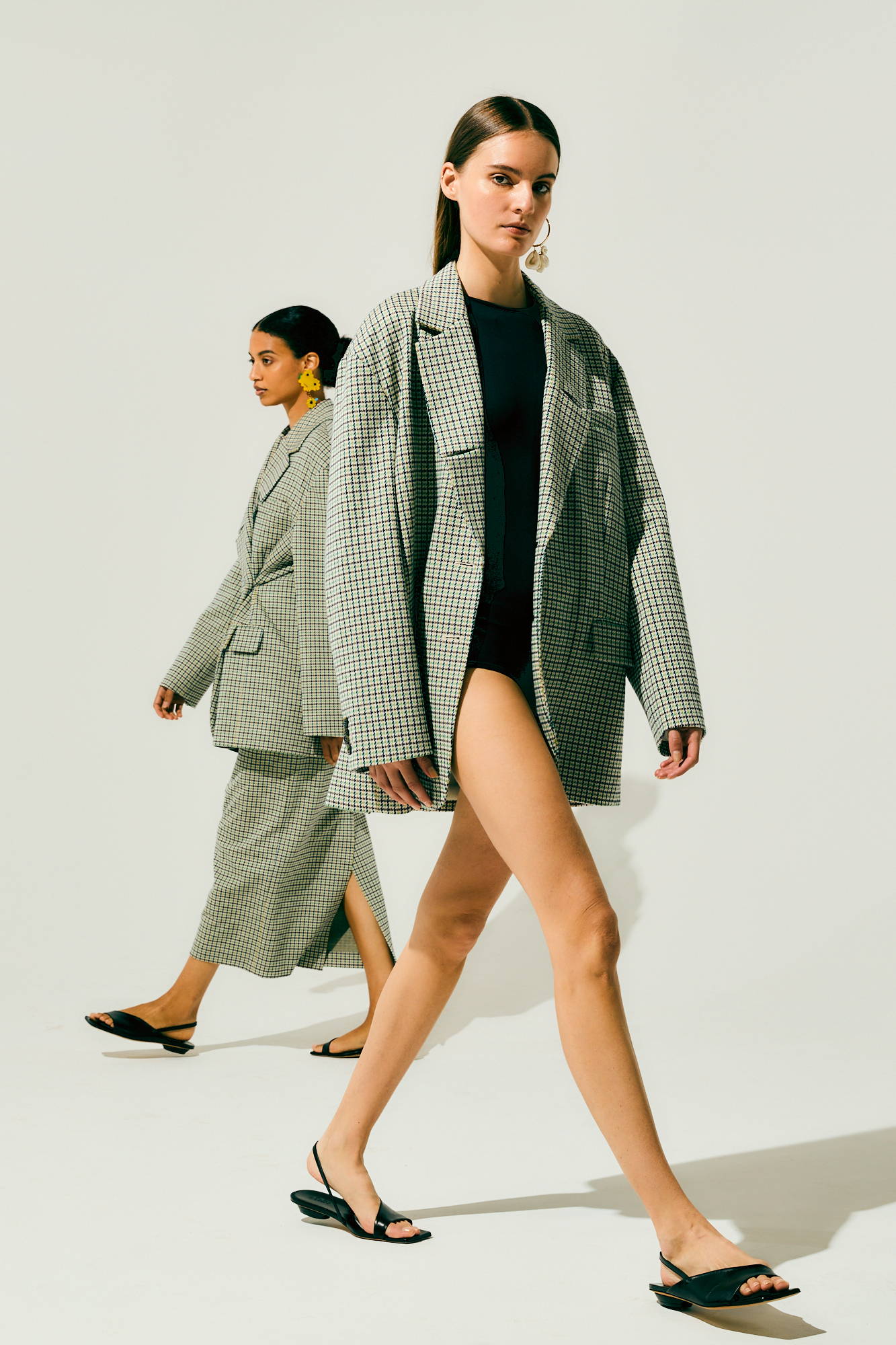 Two models walking in oversized jackets and stylish footwear.