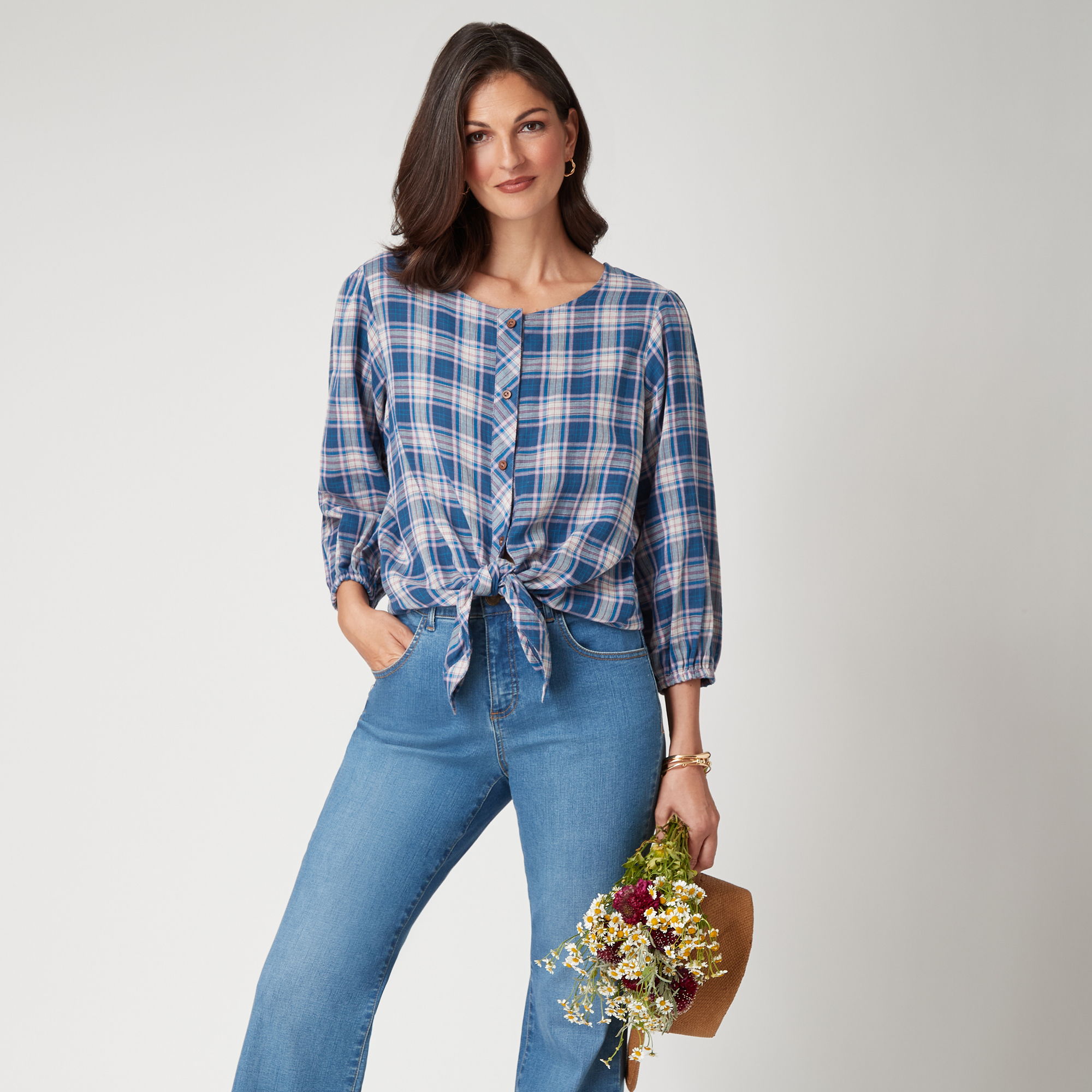 Woman in a plaid shirt and jeans, holding a bouquet of flowers.