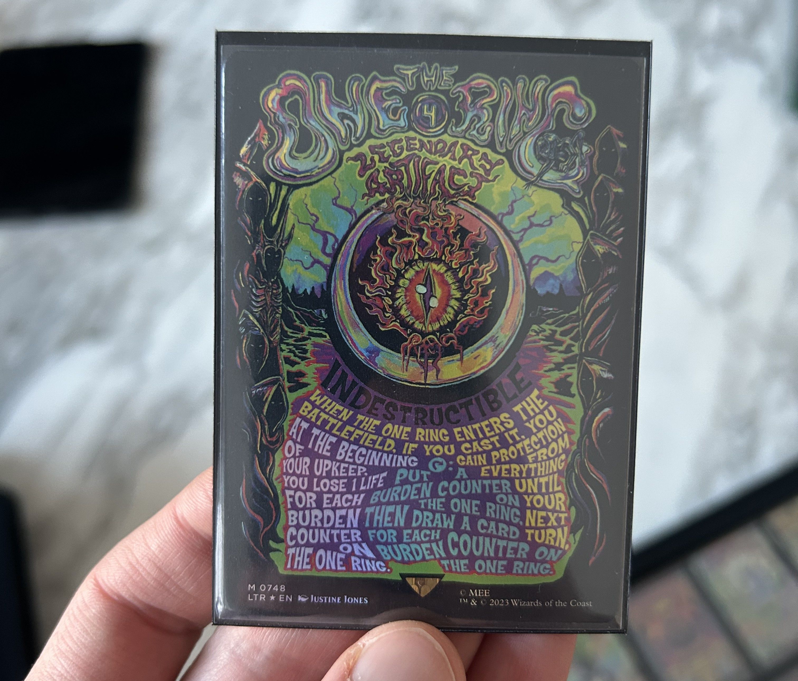 A hand holding The One Ring poster foil card with intricate designs.