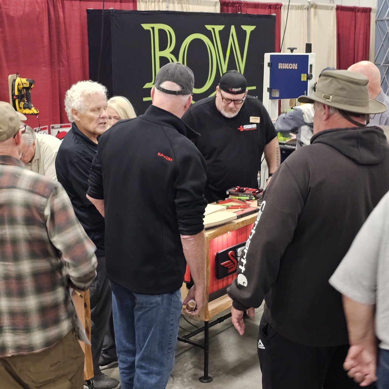 Group of people interacting at a bow convention or exhibition booth.
