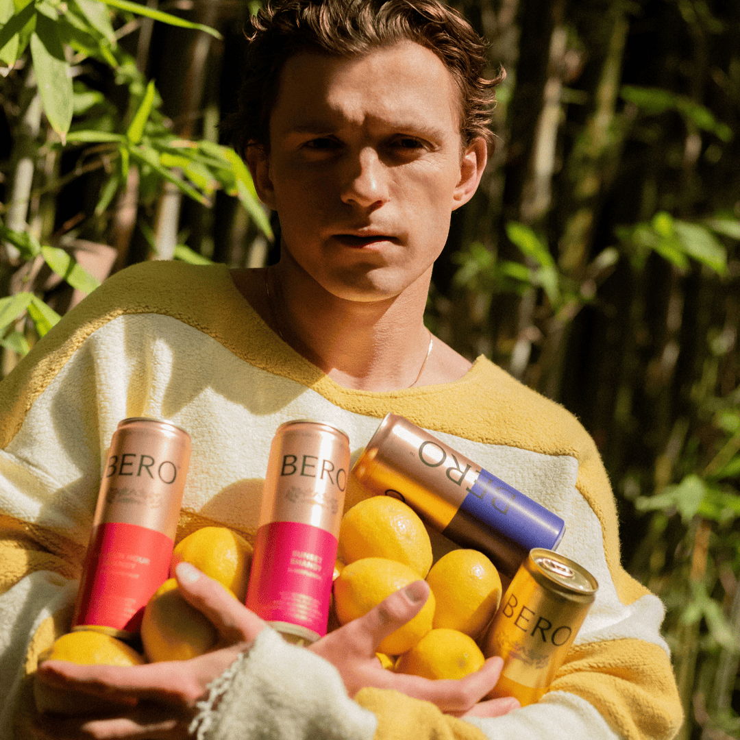 Person holding lemons and beverage cans in a bamboo setting.