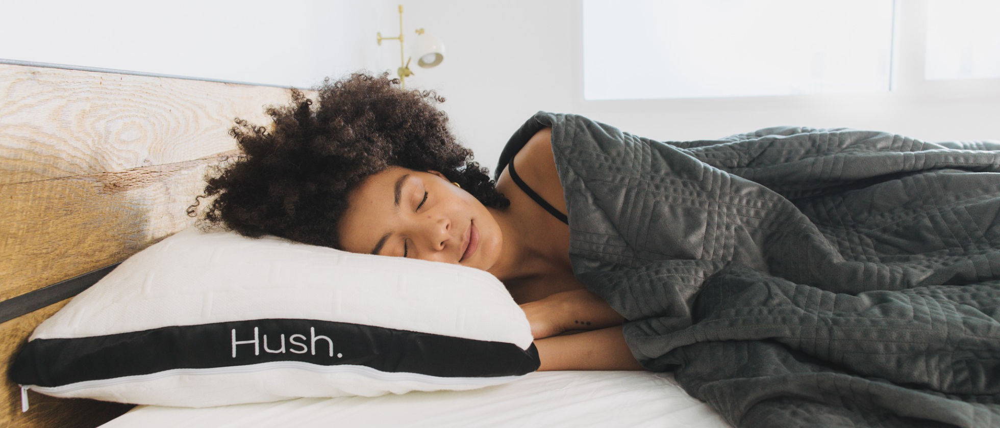 A woman sleeping on her side tucked in a Hush Classic weighted blanket.
