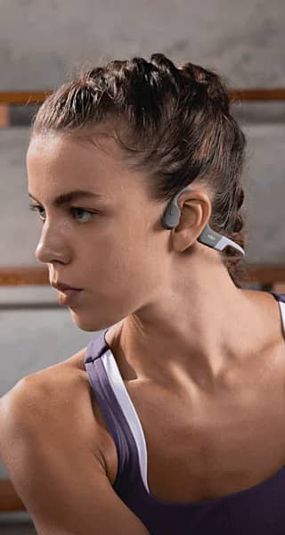 Young woman wearing open-ear sports headphones, looking to the side.