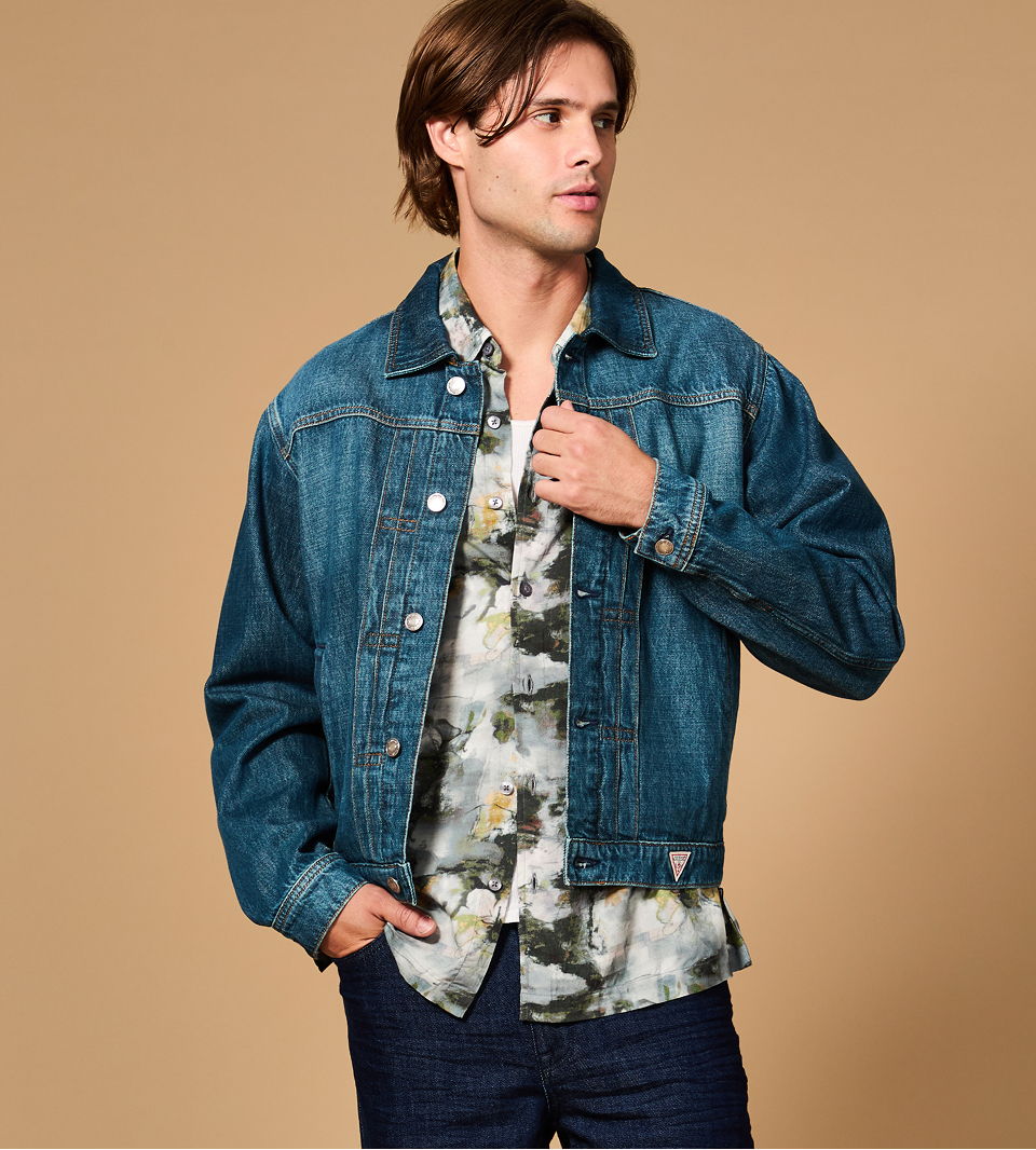 A young man wearing a GUESS denim jacket over a floral shirt.