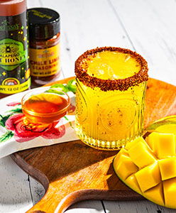 A vibrant mango mocktail with honey, spices, and fresh mango slices on a wooden board.