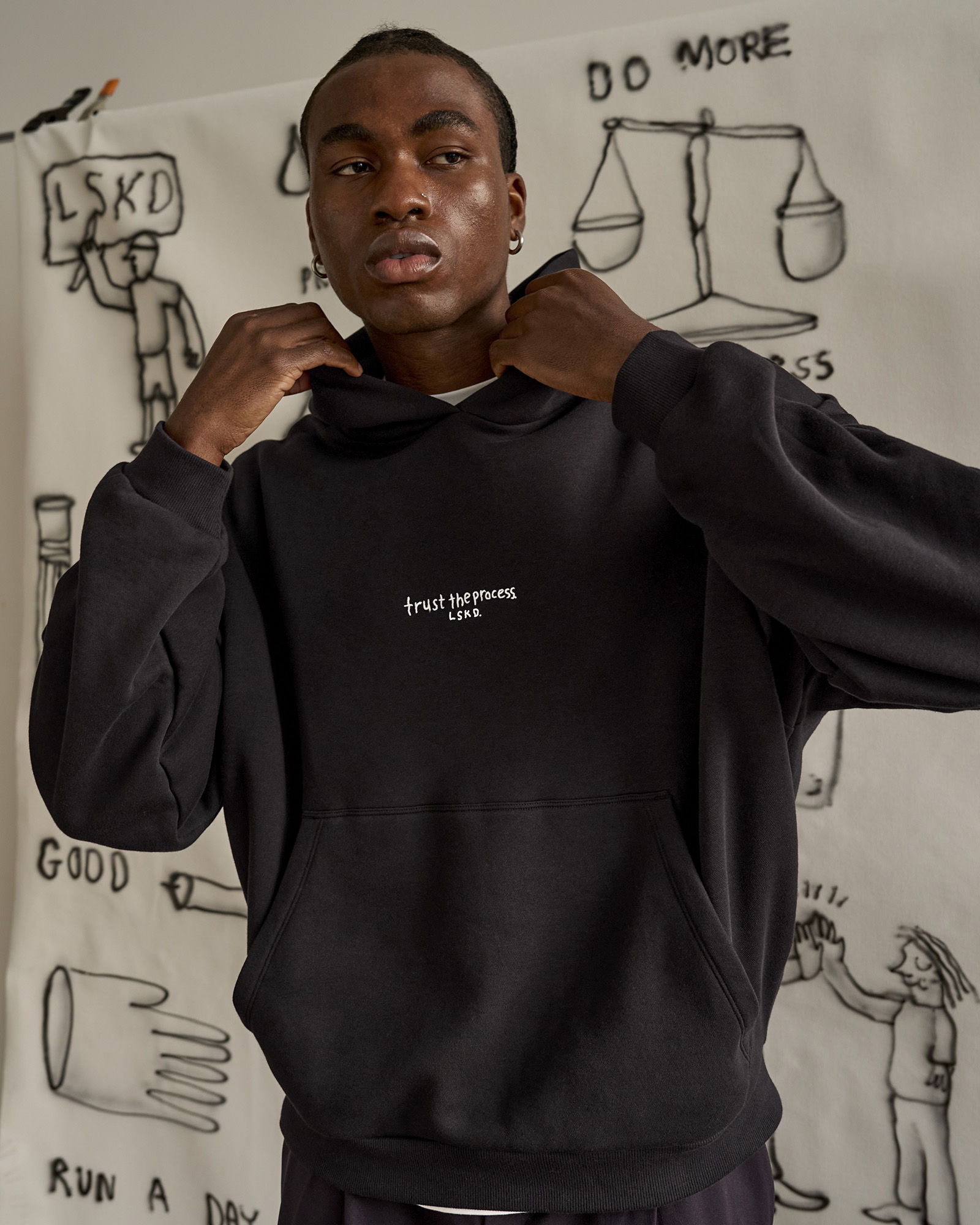 Person wearing a black hoodie in front of a drawing background.