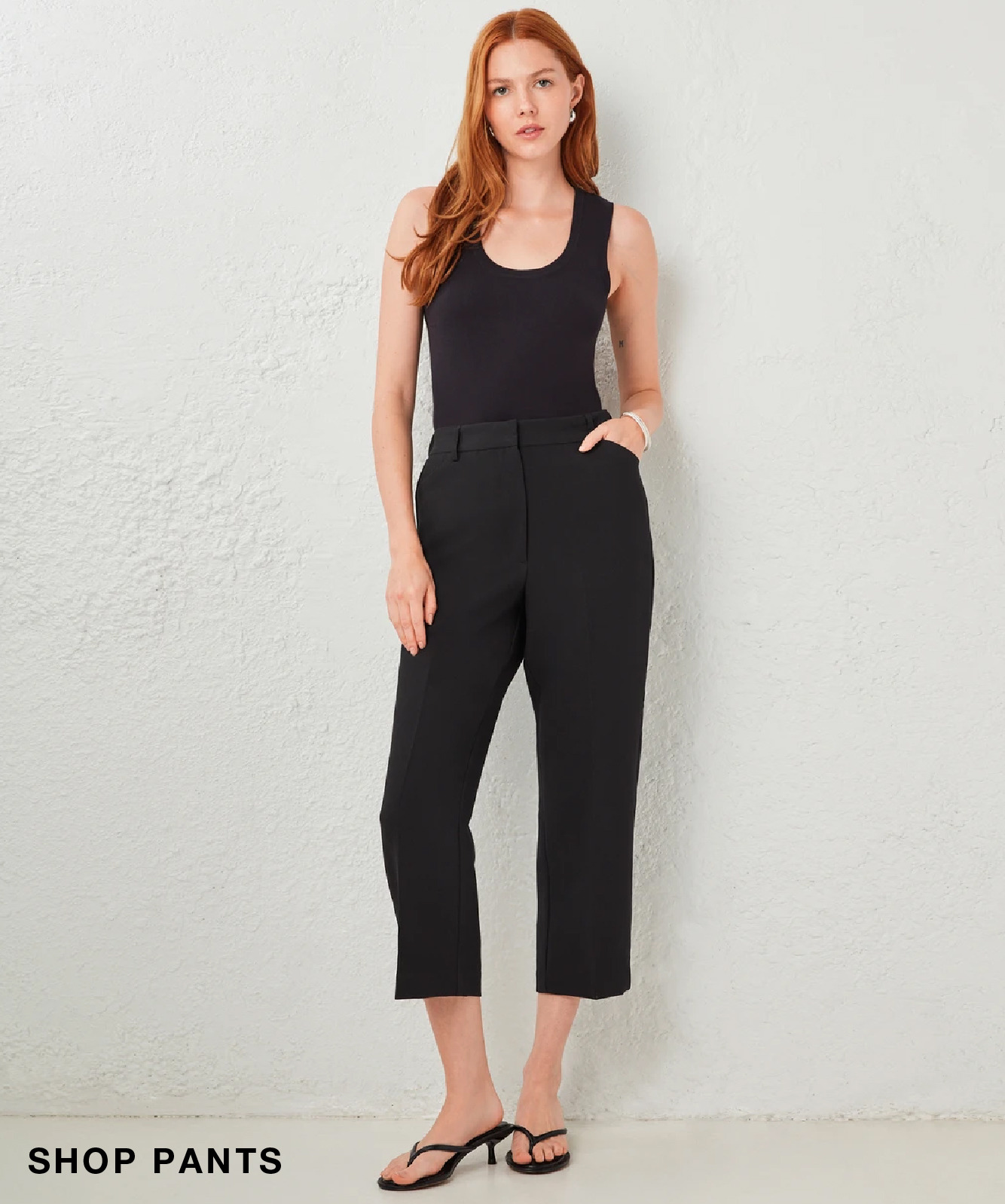 Model wearing a black tank top and black cropped pants, posing against a light background.