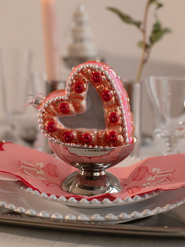A decorated heart-shaped ornament on a dinner plate with glassware.