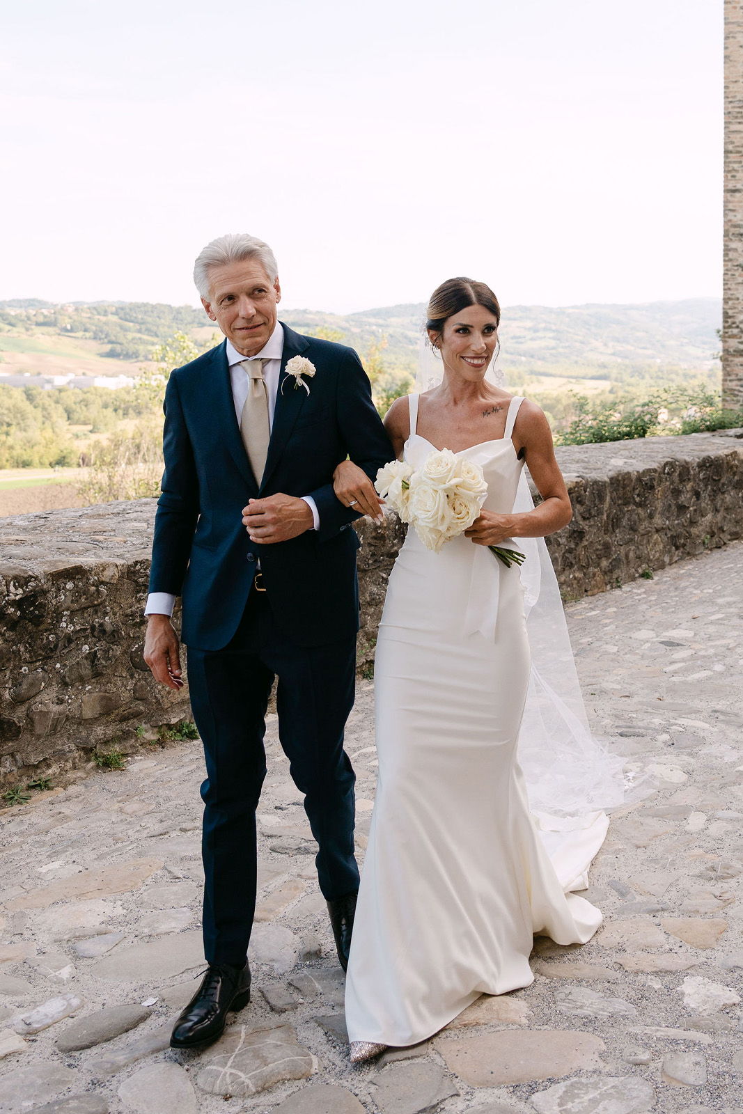 Bride and groom walking together outdoors, surrounded by scenic landscape.