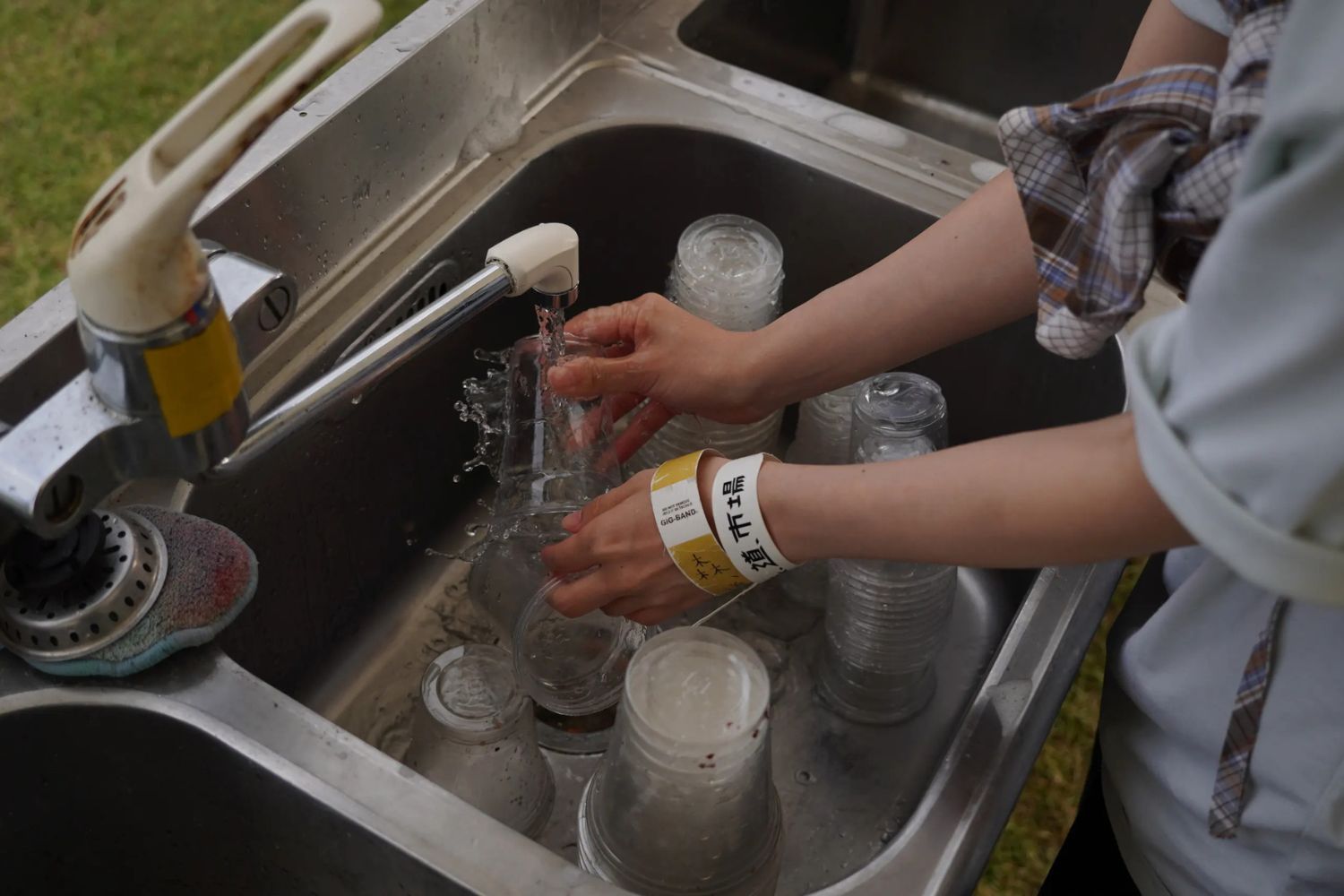 Person washing glasses in a sink with running water.