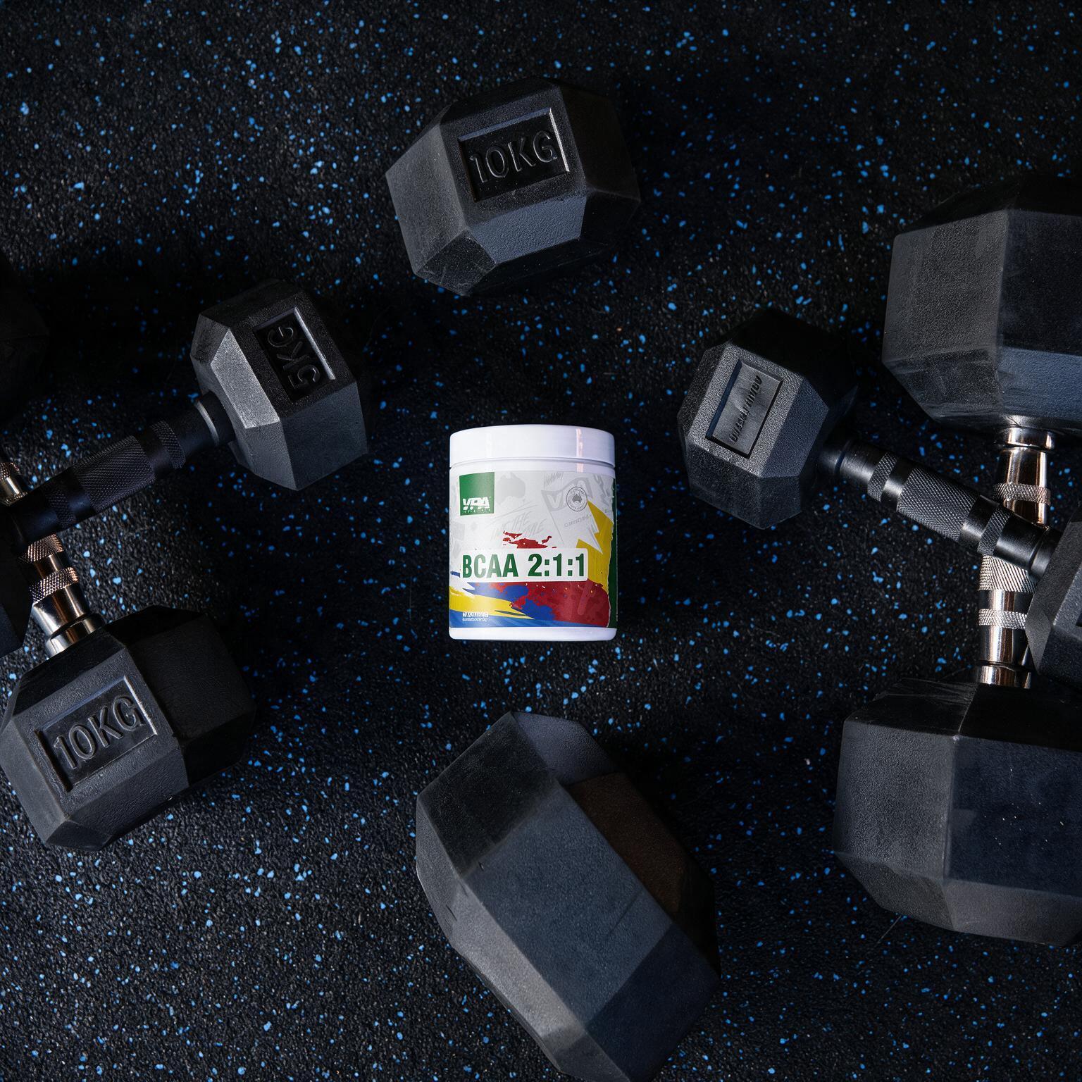 Dumbbells surrounding a container of fitness supplement on a dark surface.