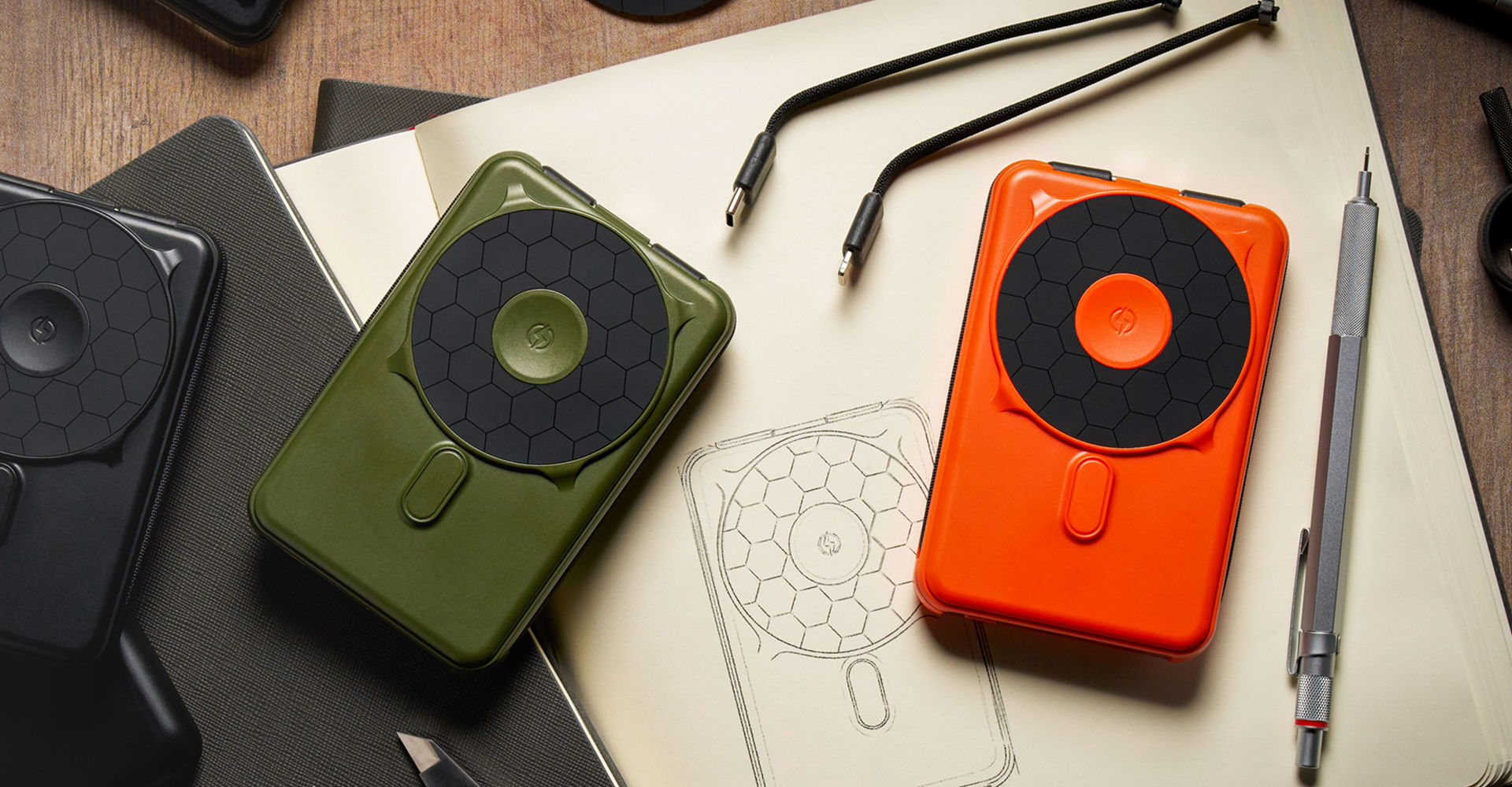 Two portable speakers in green and orange on a desk with tools and sketches.