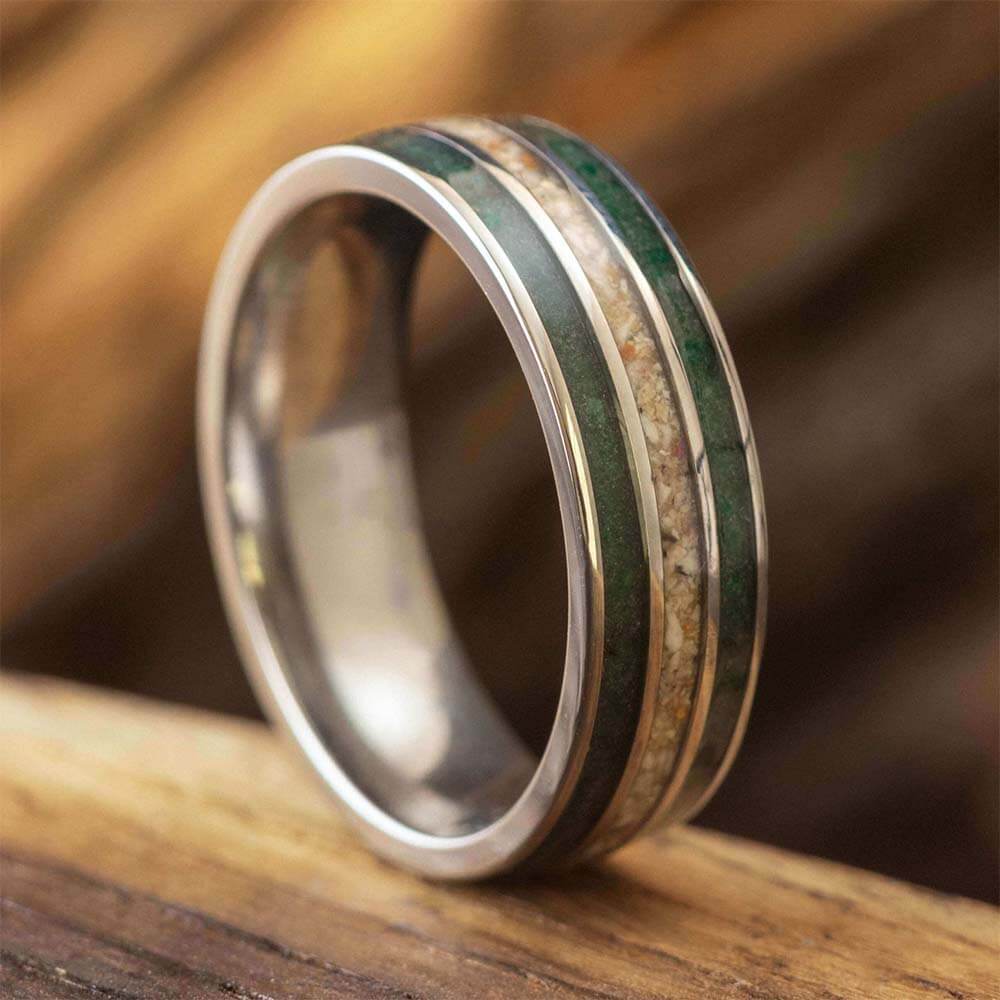 A metallic ring with green and brown inlays on a wooden surface.