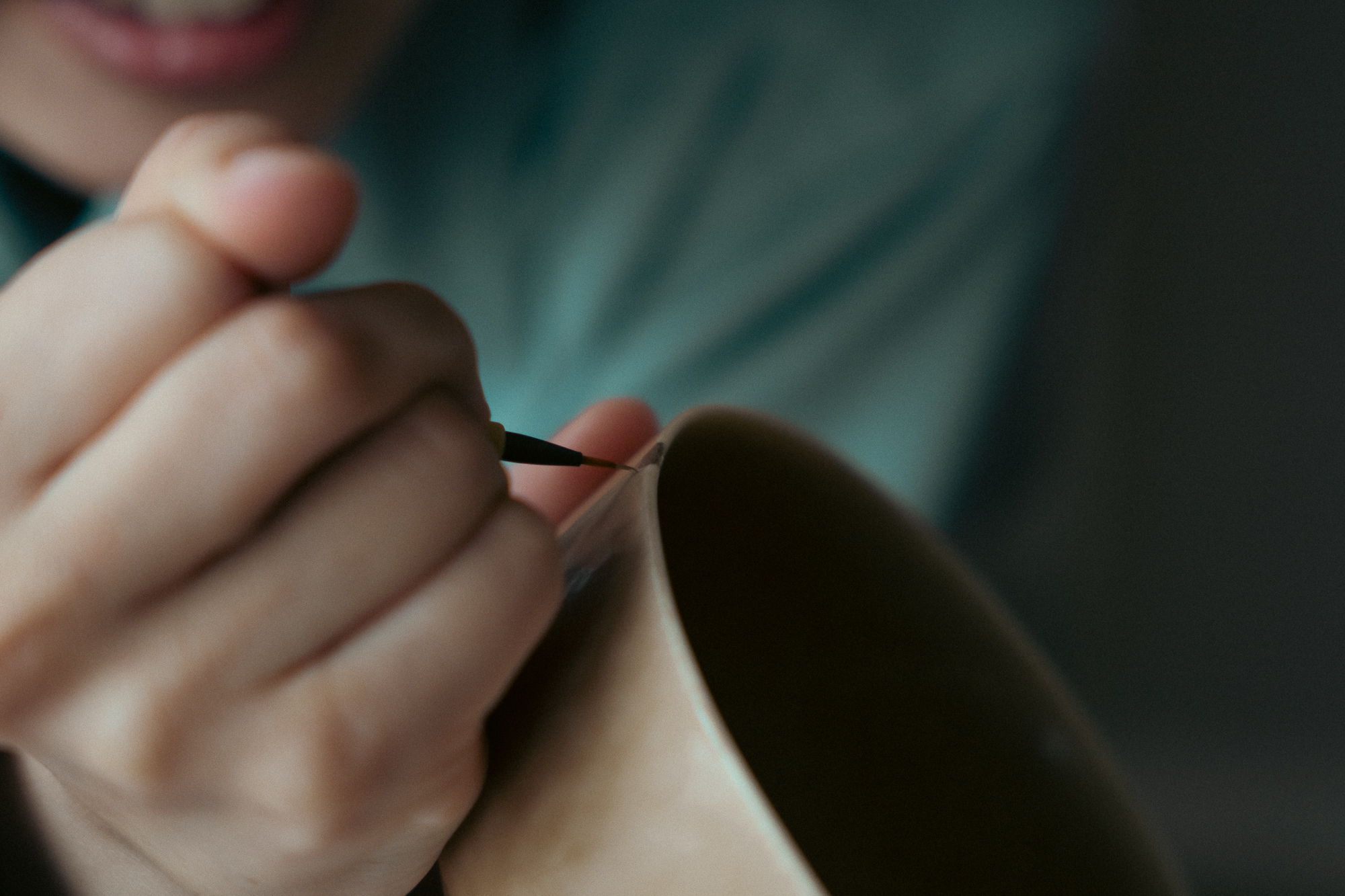 A person painting a ceramic bowl with a small brush.