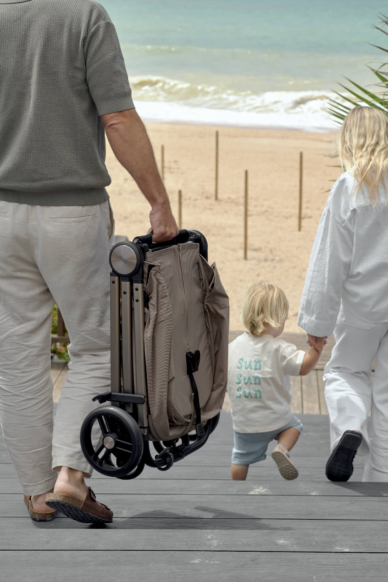 Person carrying a stroller walking with two children on a beach.
