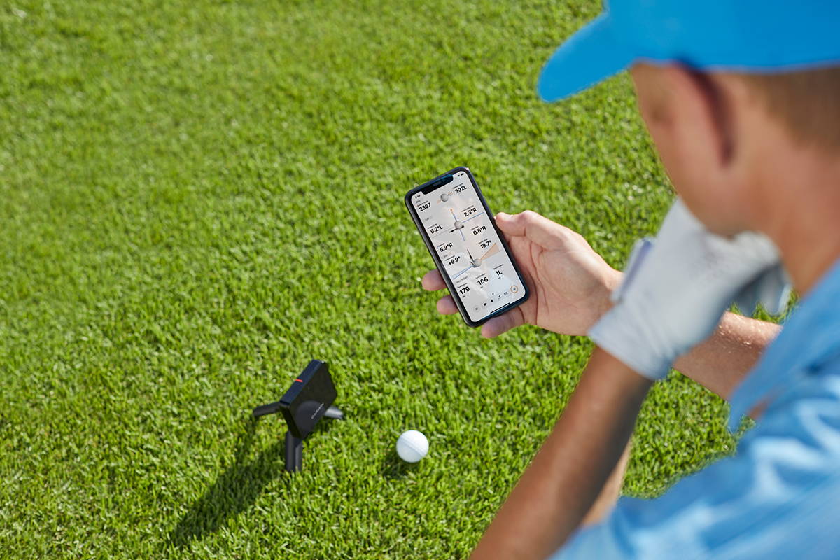 A golfer looking at the Garmin Golf app on the golf course over the Garmin Approach R10