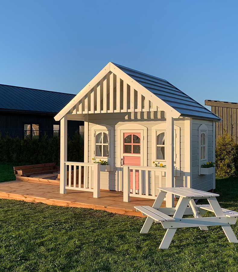 Custom playhouse  with large terrace on grass with blue sky in the back by WholeWoodPlayhouses