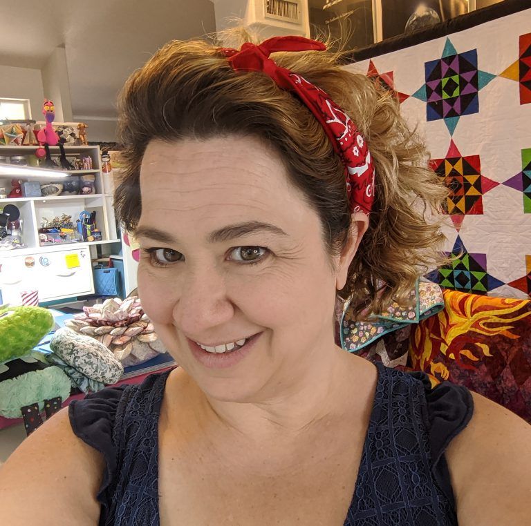 Smiling person with curly hair and red bandana in a colorful room.