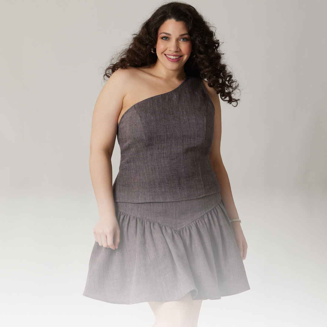 A woman wearing a one-shoulder gray dress, smiling at the camera.