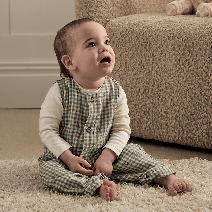 A child sitting on a rug, looking up with a cheerful expression.