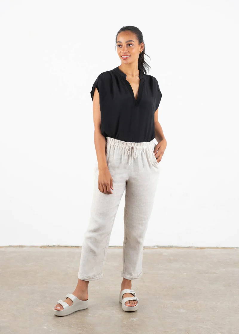 A model wearing a black top with short sleeves and oatmeal coloured tapered linen trousers with off white chunky platform slides
