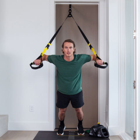 Person performing a TRX exercise in a home gym setting.