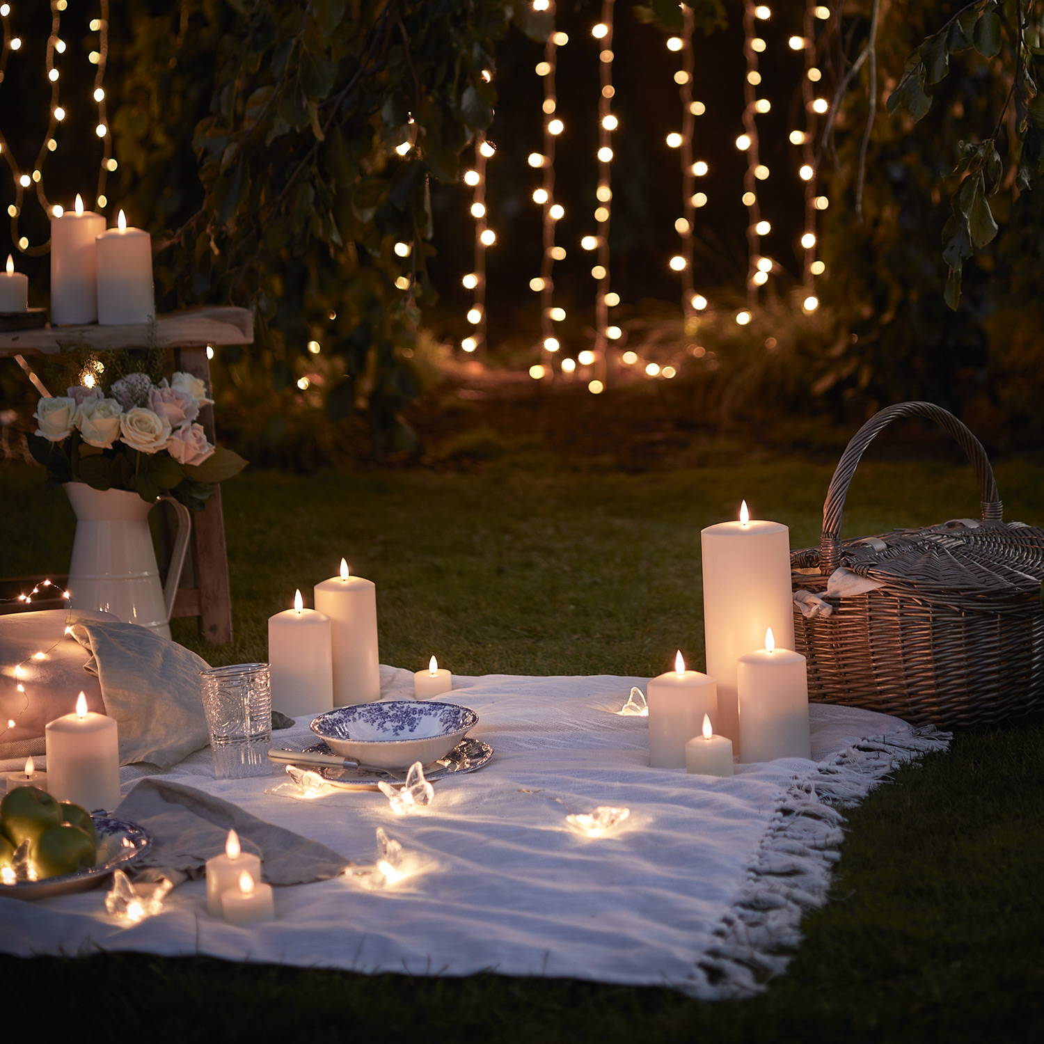 Gros plan sur un pique-nique nocturne avec des bougies LED, des guirlandes lumineuses et des rideaux lumineux.