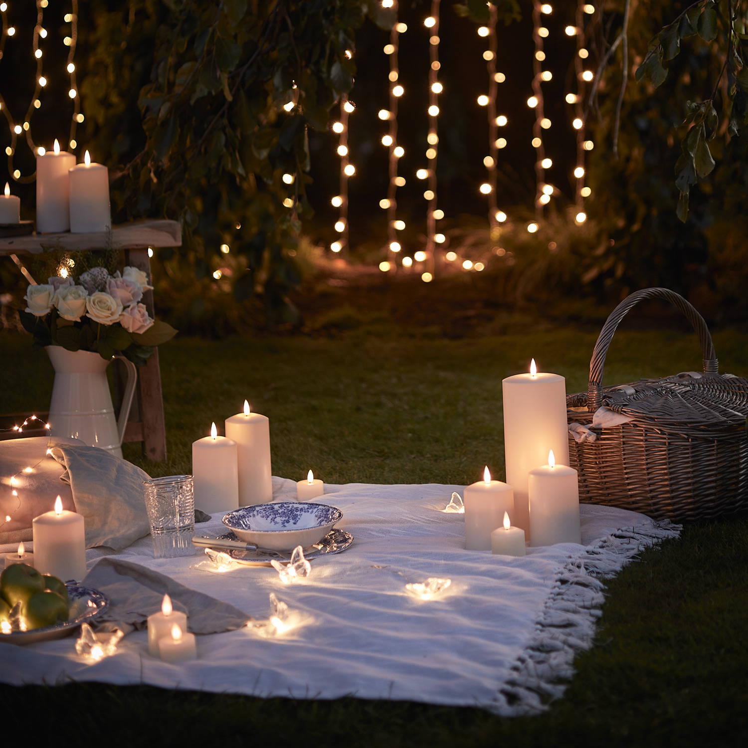A cosy close up of a night time picnic with LED candles, fairy lights and curtain lights.