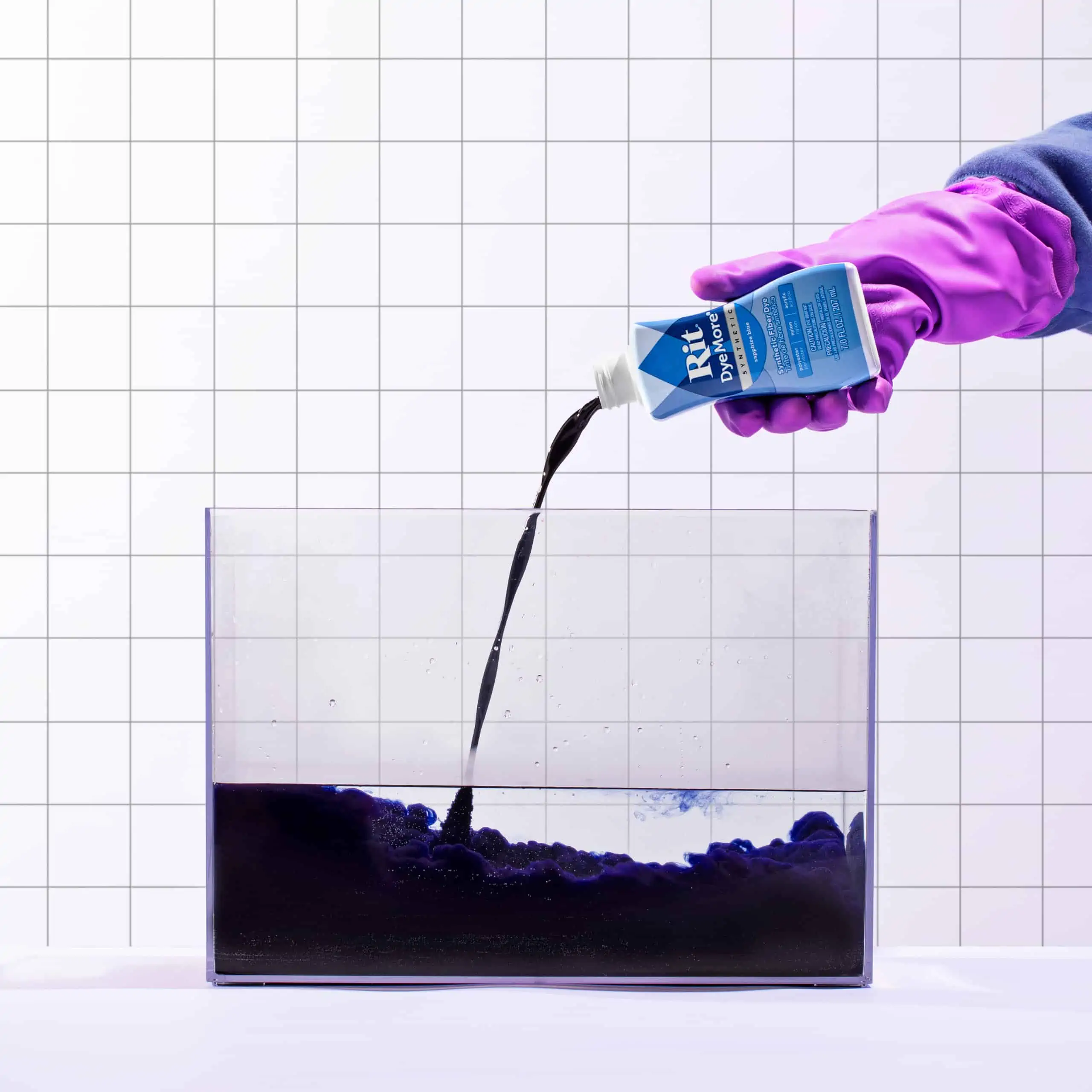 Person in gloves pouring liquid into a clear container filled with dark fluid.