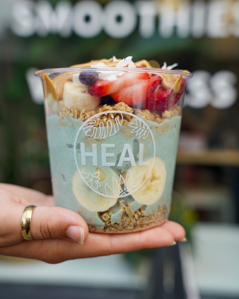 A hand holding a cup of colorful smoothie bowl with fruits and granola.