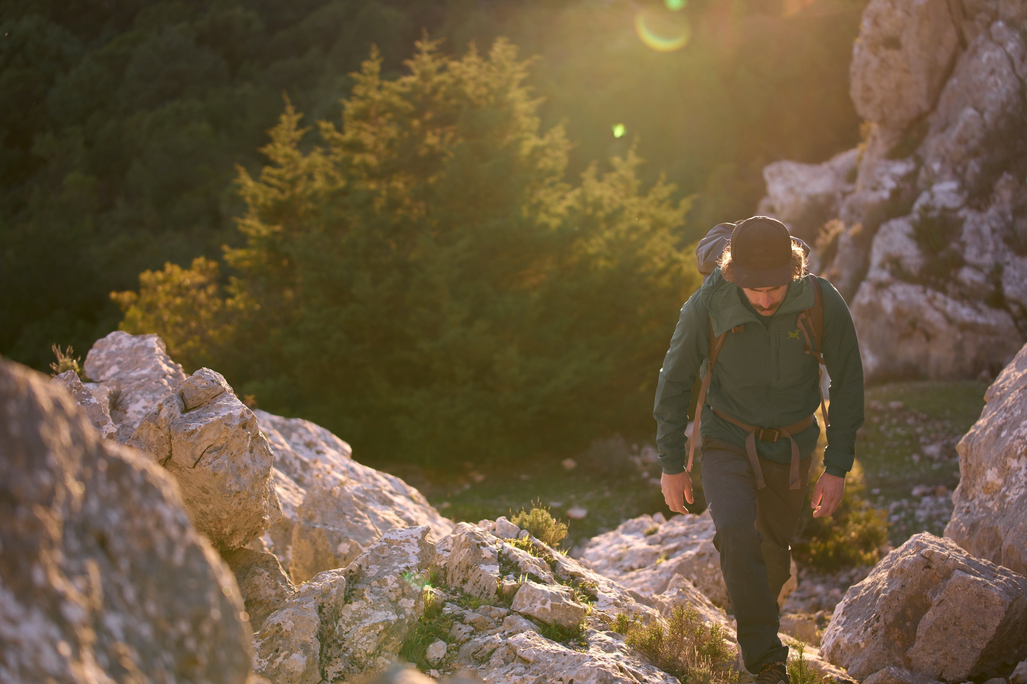 Hiker climbing rocky terrain during sunset, surrounded by nature.