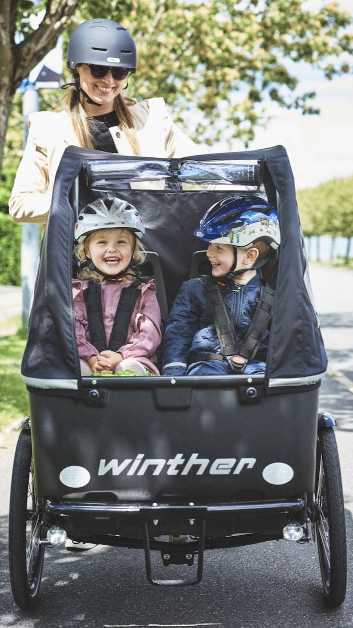 Two children in the Winther Cargoo front box with rain cover