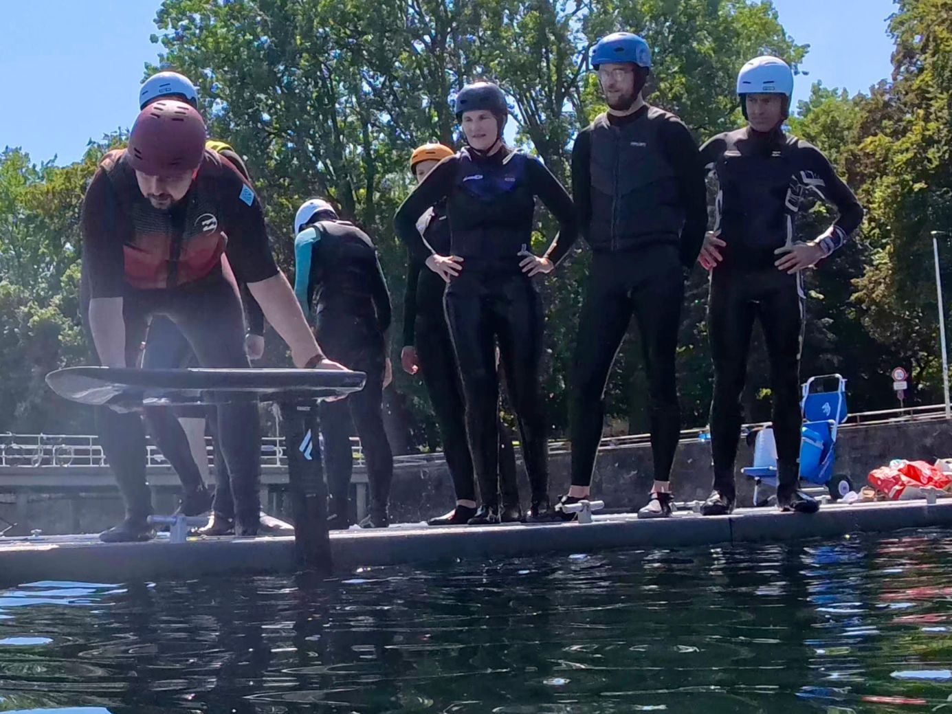 Group of people in wetsuits preparing for water activities at a dock.