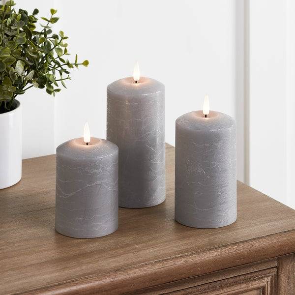 3 Grey LED candles on a bedside table in a white room.