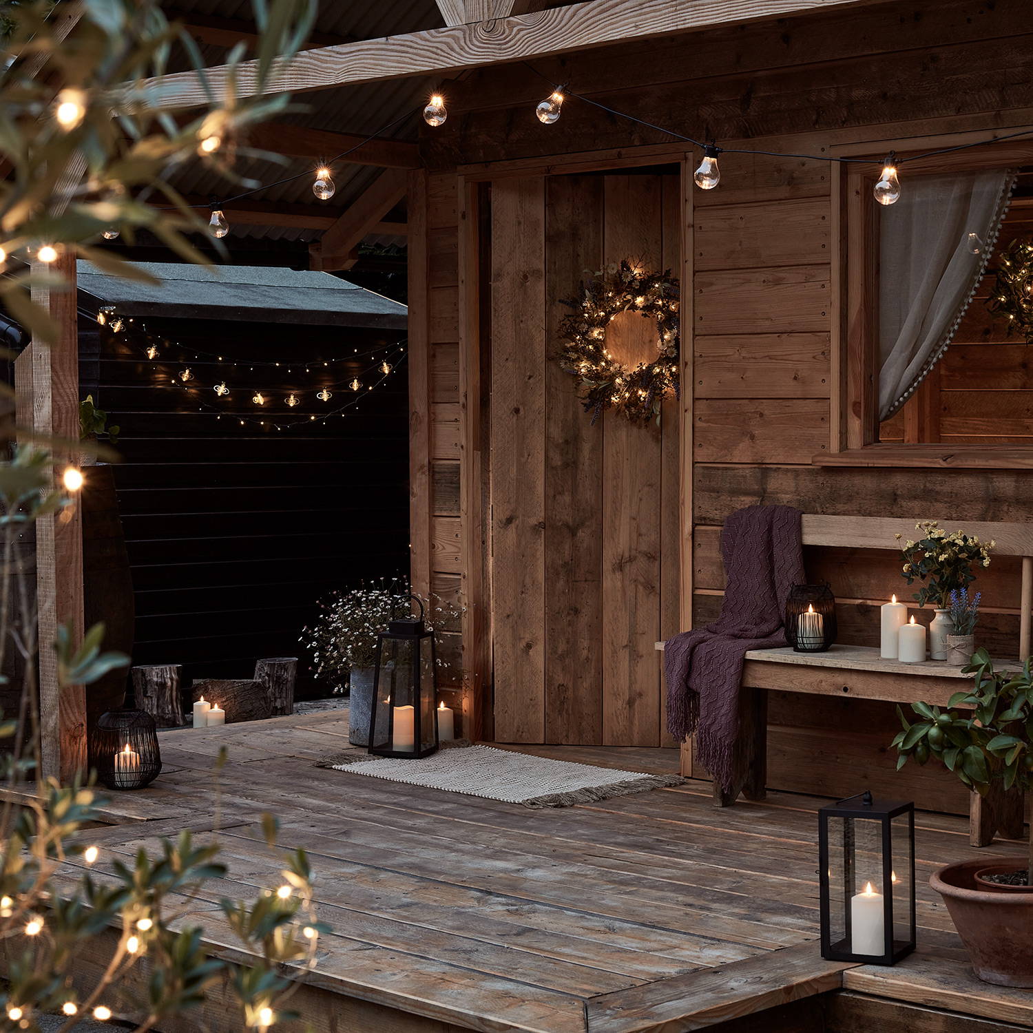 An outdoor summerhouse decorated with a wreath, lanterns, LED candles and warm white Core Connect festoon lights.