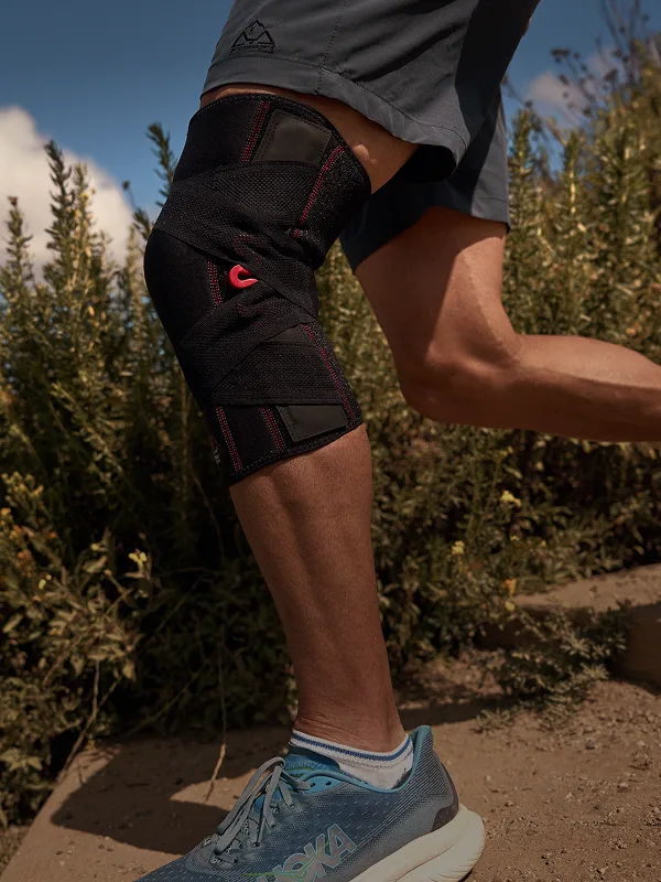 Person running with a knee brace and athletic shoes in an outdoor setting.