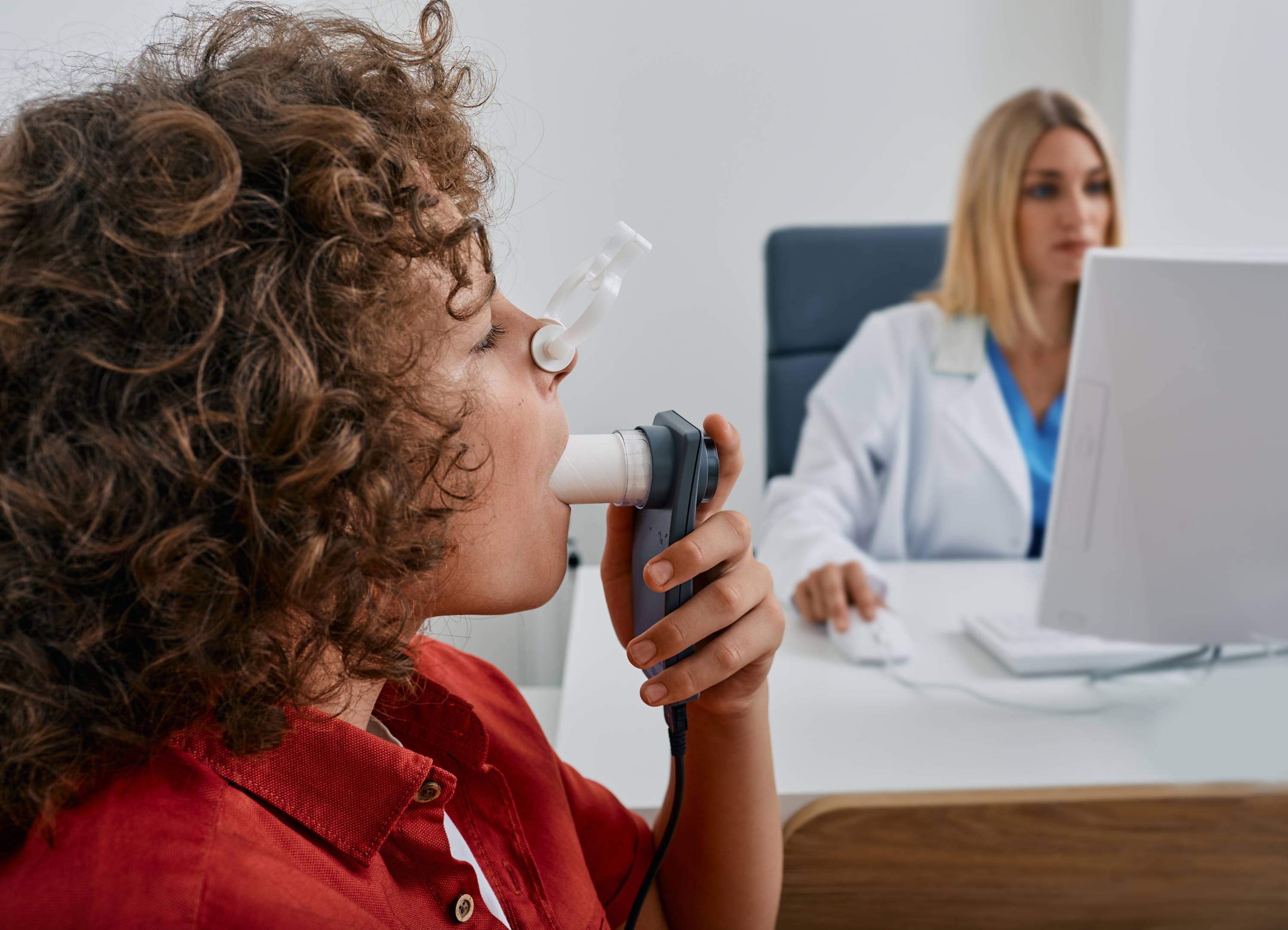 Kind bij de dokter krijgt een longfunctietest voor astma. Het kind draagt een neusclip en blaast in een buis.