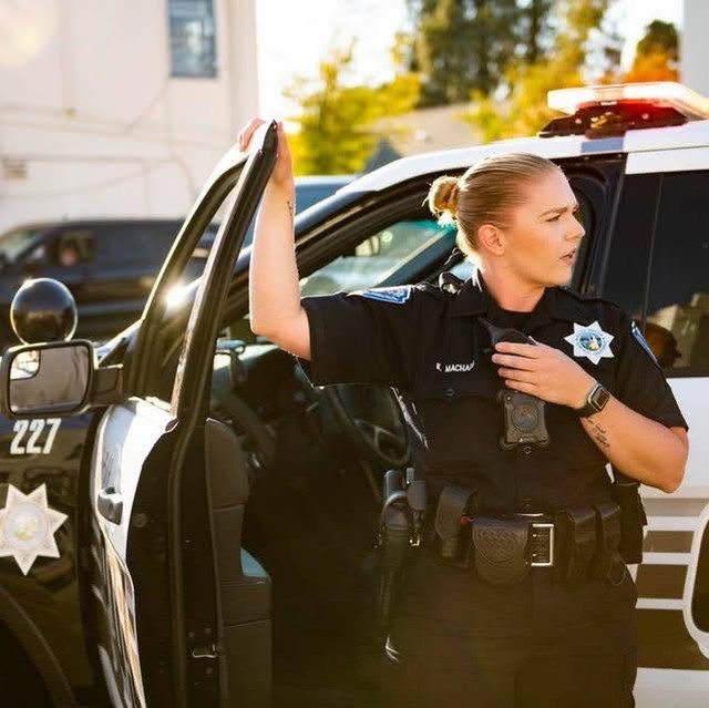 A police officer standing by a patrol car, looking thoughtful.