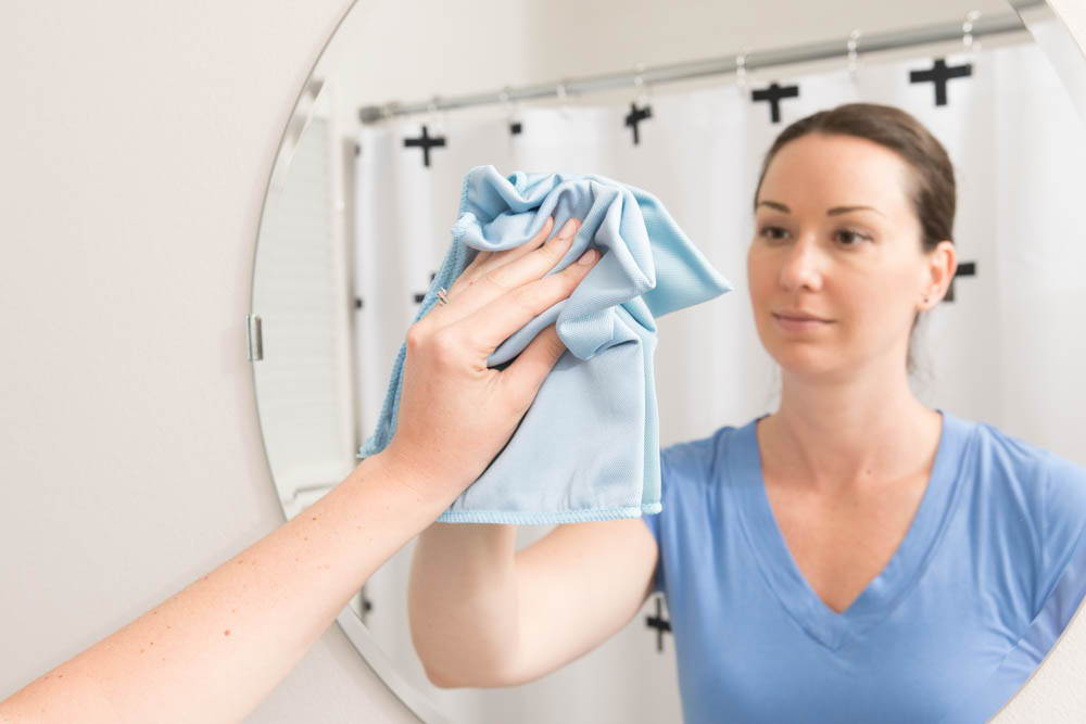 woman cleaning mirror with blue microfiber towel