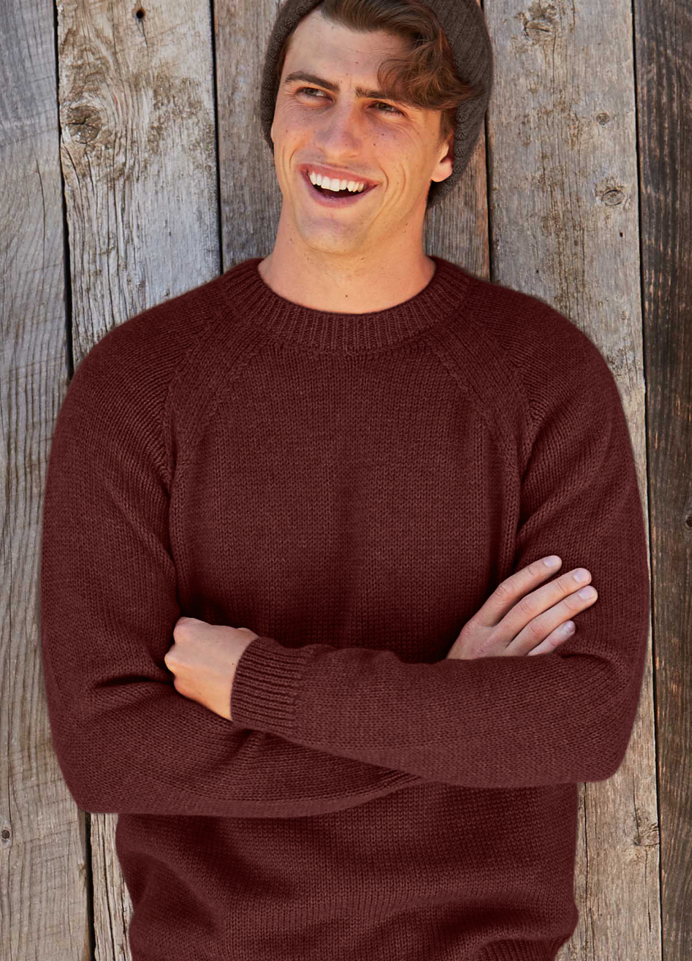 Smiling man in a brown sweater against a wooden wall.