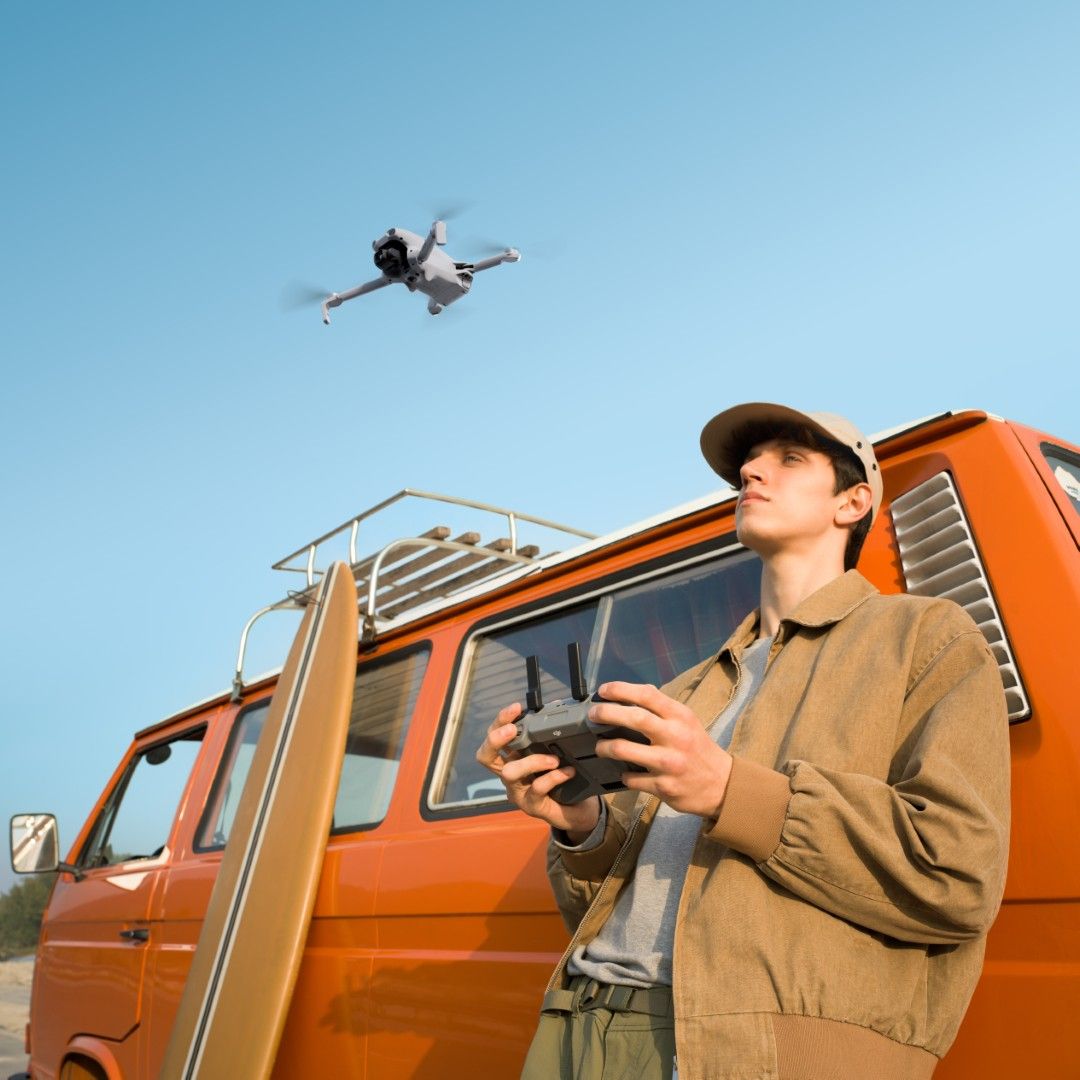 A person controls a DJI Lito X1 drone near an orange van under a clear sky.