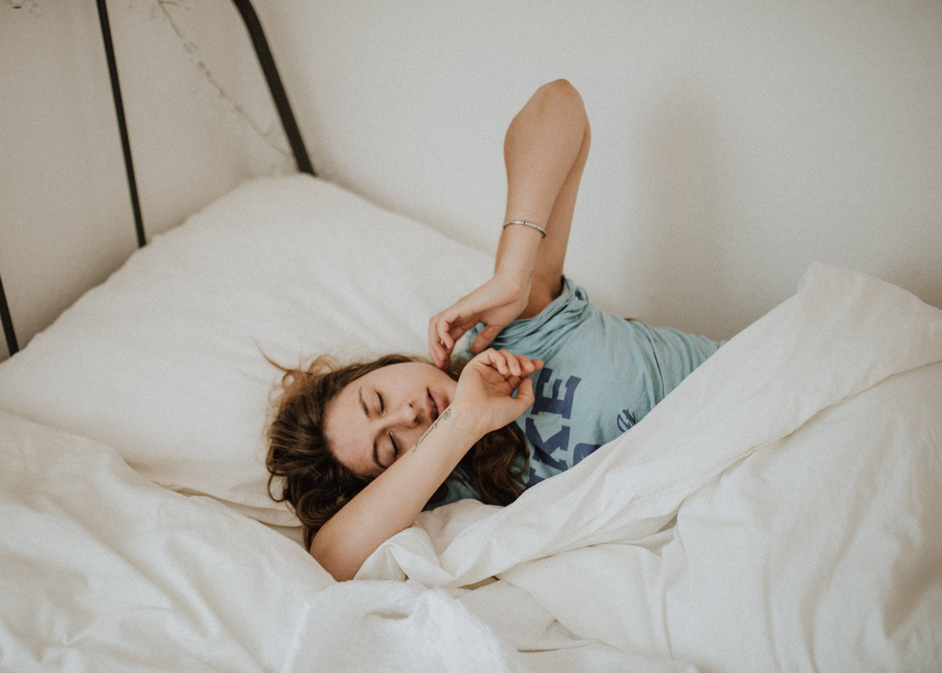 A woman lies in a white bed and reaches one elbow into the air.