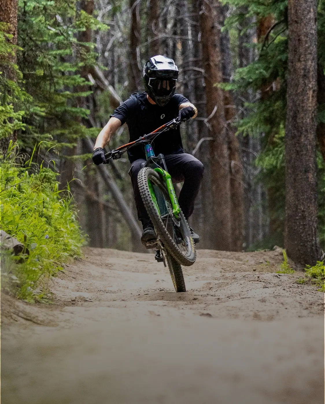 Mountain biker coming down a dirt trail and doing a wheelie while wearing a PEARL iZUMi MTB jersey