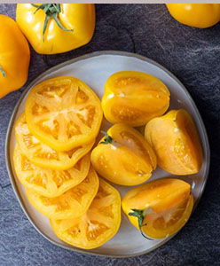 A plate of sliced yellow tomatoes with whole tomatoes beside it.