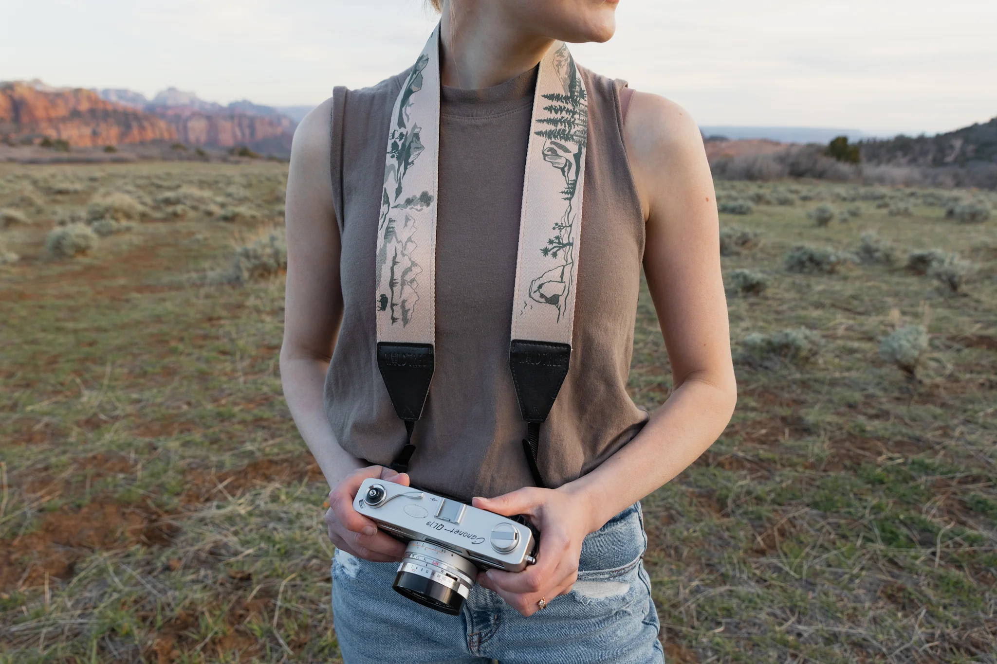 Woman wearing a national park inspired neck camera strap outdoors in the desert. 