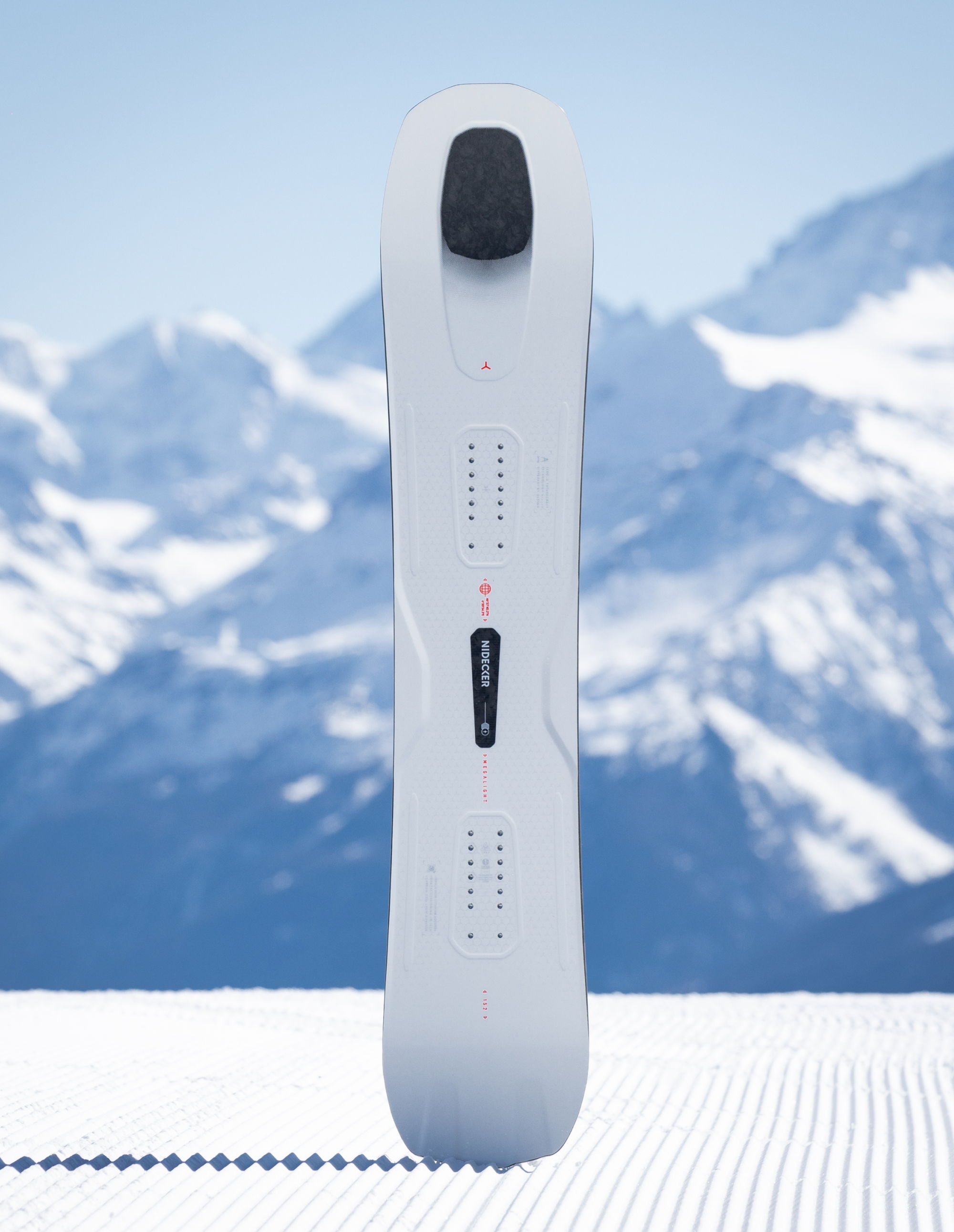 White snowboard standing on snow with mountains in the background.