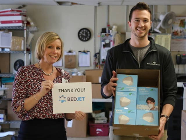 Two healthcare workers pose with a box of N95 masks and a sign that says 