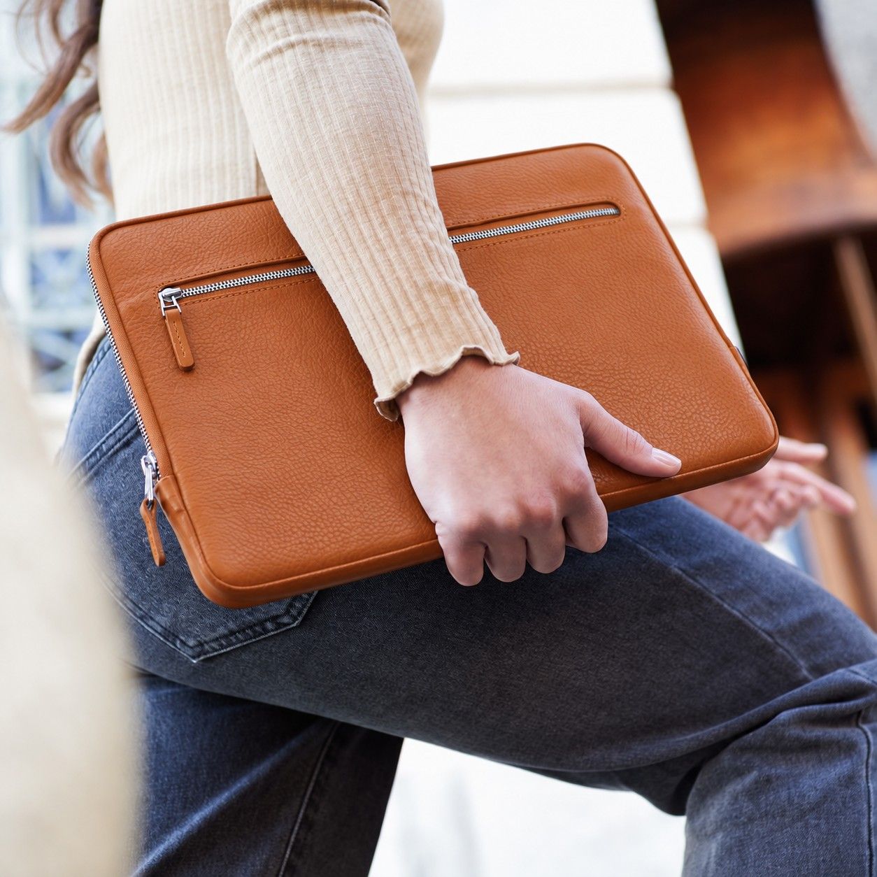 Eine Frau trägt eine iPad Pro Hülle aus hellbraunem Leder unter dem Arm