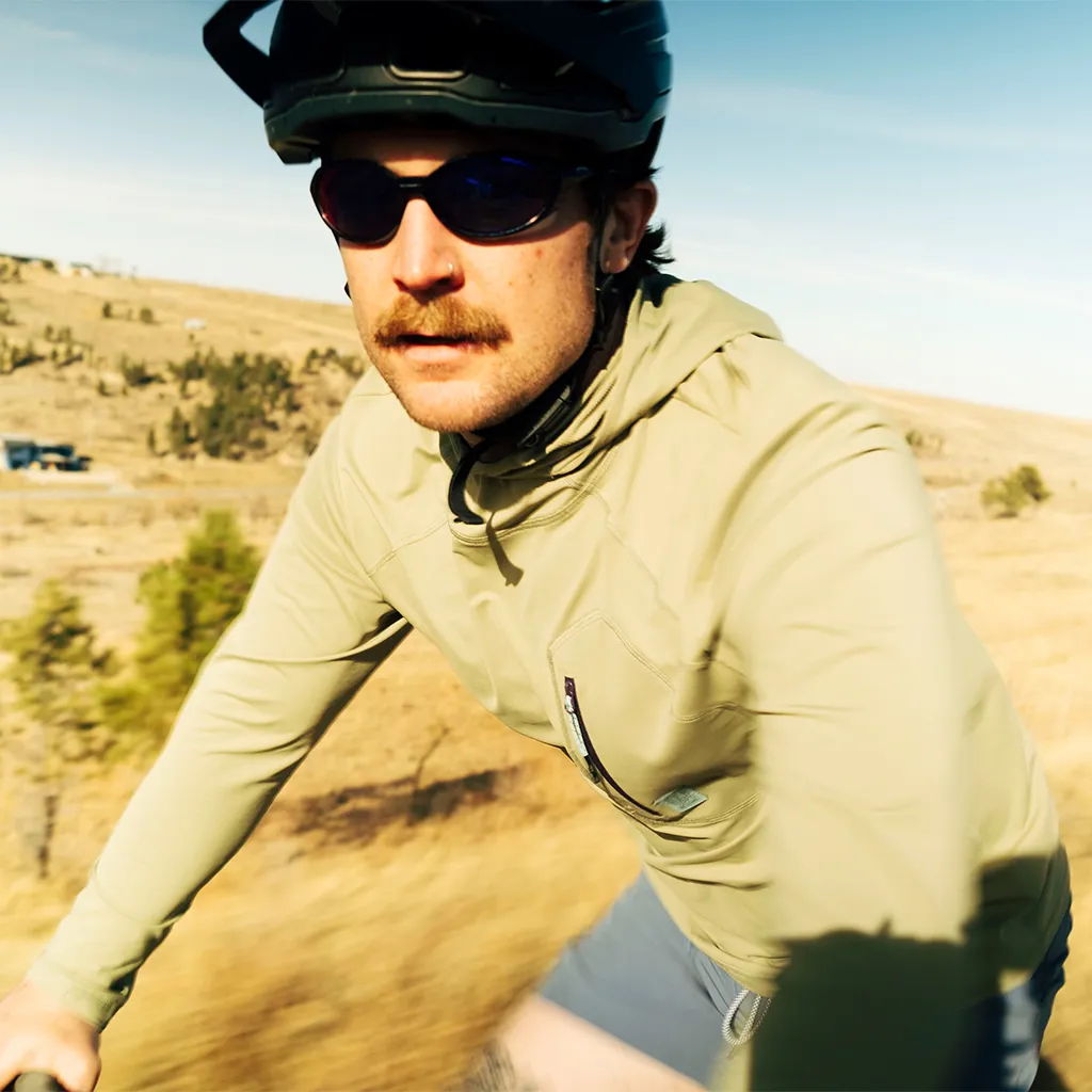A cyclist wearing sunglasses and a helmet, riding outdoors on a sunny day.