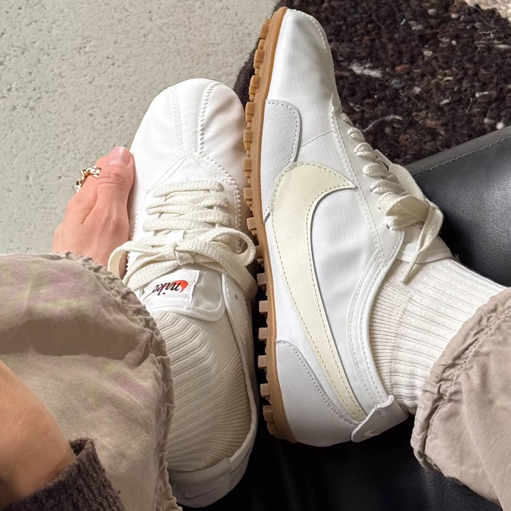 A person wearing white Nike shoes with textured soles and beige pants.